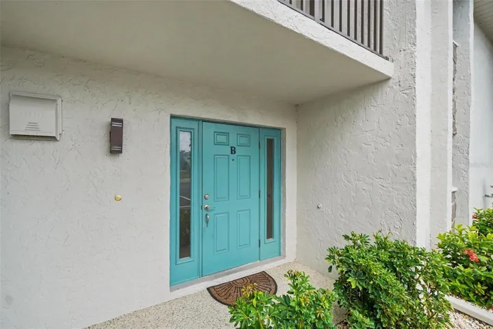 Front entry to unit B with a turquoise front door, covered walkway, and tropical landscaping at this Punta Gorda waterfront condo.