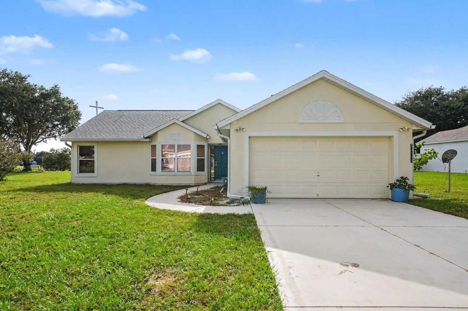 Cream-colored home with attached garage and circular front walkway on spacious lawn
