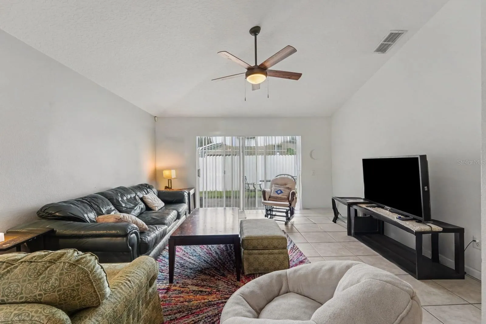 Spacious living area with vaulted ceiling, tile flooring, and sliding glass patio doors