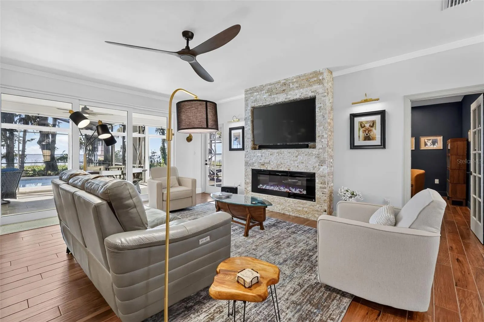 Living room with stacked stone electric fireplace, crown molding, updated fixtures and gleaming wood-like tile floors