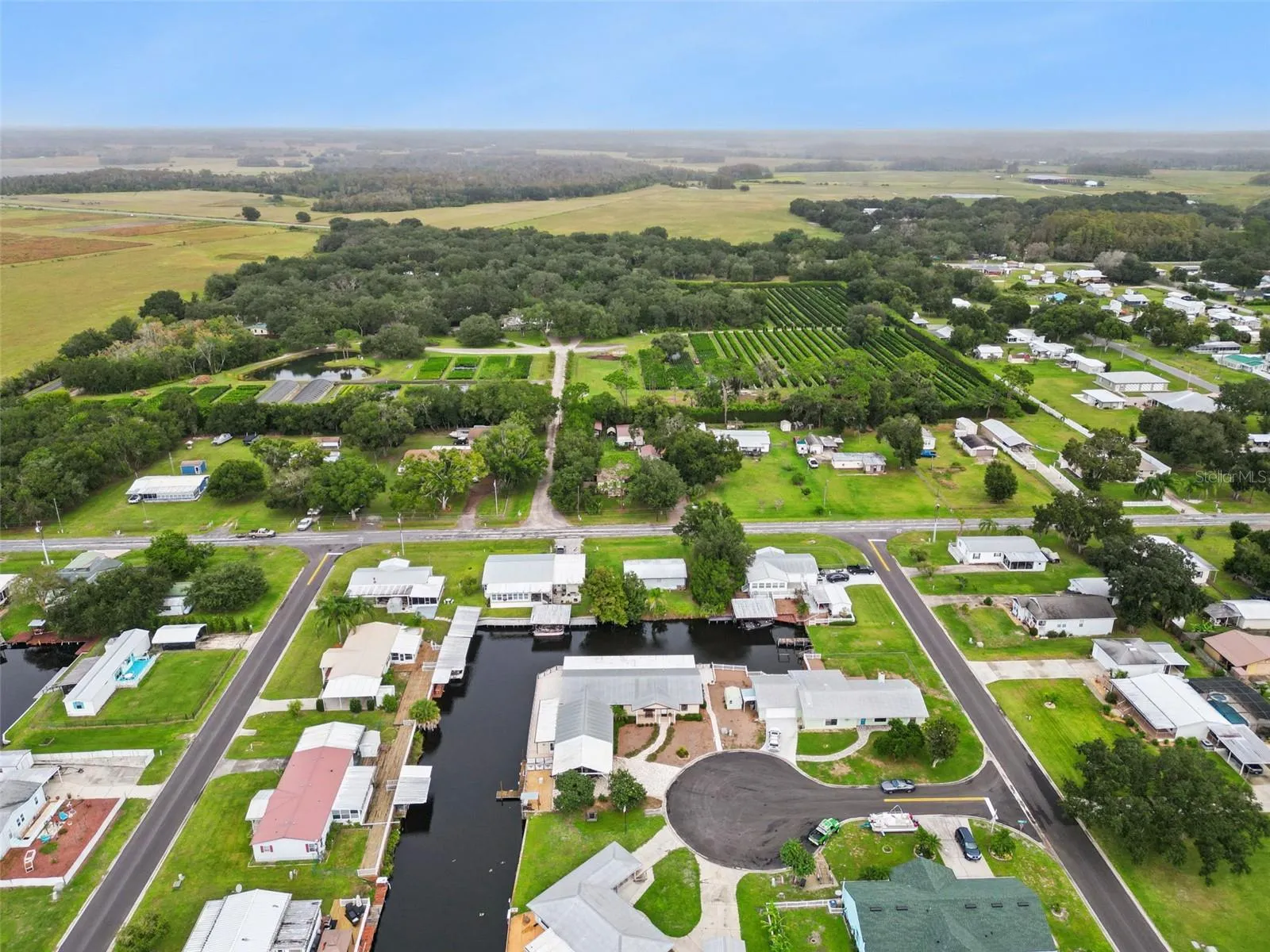 Aerial Community & Countryside View: Broad high-altitude aerial view showcasing the home's cul-de-sac position within the quiet canal community, backed by lush green pastureland.