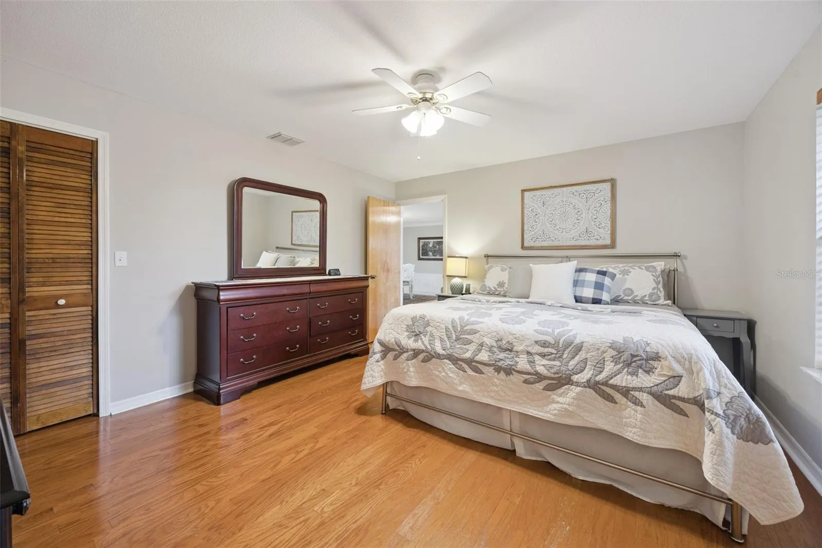 Primary Suite Storage View: Alternate perspective of the primary bedroom detailing a large louvered closet, rich wood laminate flooring, and ample space for king furniture.
