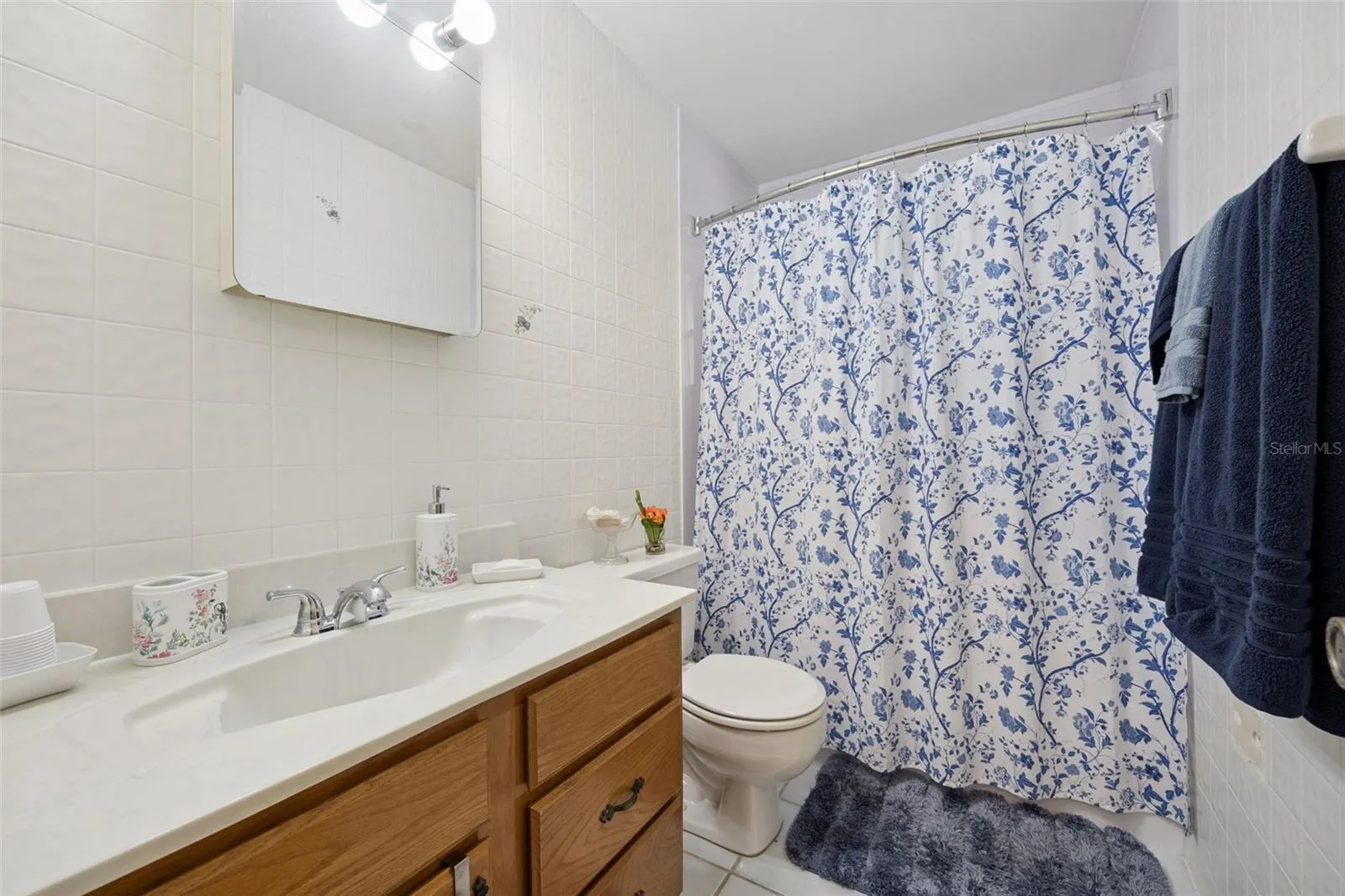 Guest Bathroom: Full secondary bathroom equipped with an oak vanity, tub/shower combination with decorative curtain, and neutral wall tile.