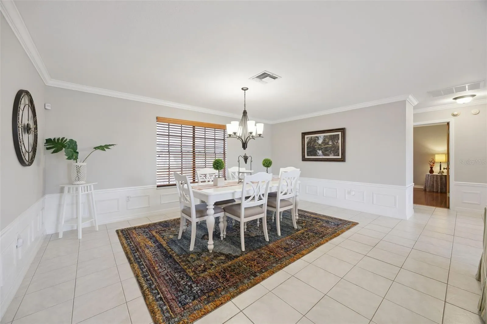 Formal Dining Room: Elegant formal dining area featuring classic wainscoting paneling, crown molding, a central chandelier fixture, and tiled flooring.