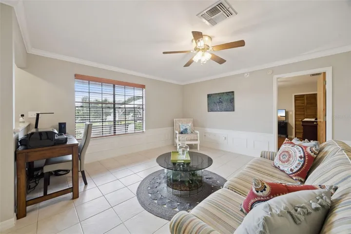 Living Room Workspace: Living area overview highlighting a dedicated desk nook along a half wall, ceramic tile flooring, and natural light from a large front window.