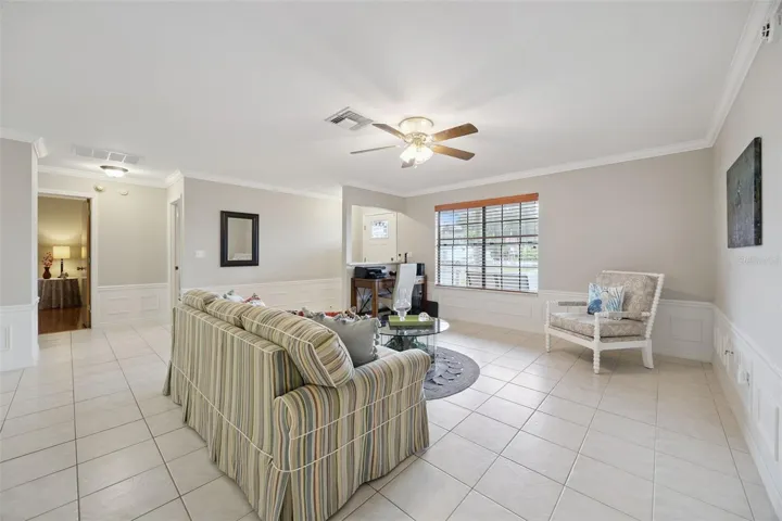 Living Room Corner: Comfortable living room layout showcasing light tiled floors, wall wainscoting, a ceiling fan, and views toward adjacent entry areas.