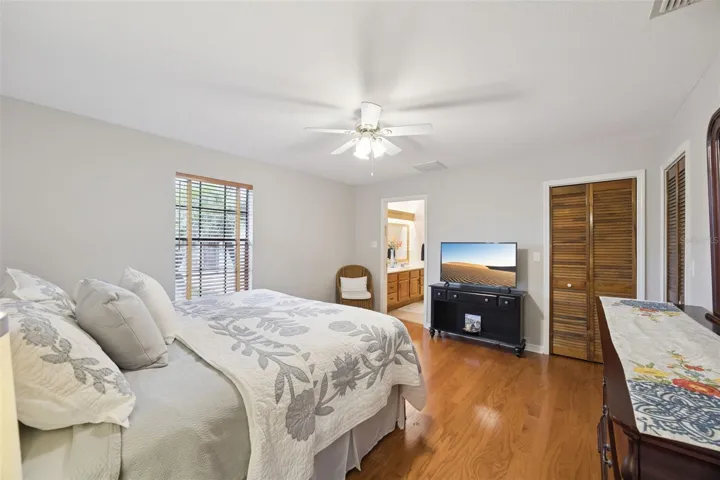 Primary Bedroom Suite: Spacious primary bedroom featuring warm wood laminate flooring, ceiling fan, louvered closet doors, and access to an ensuite bathroom.