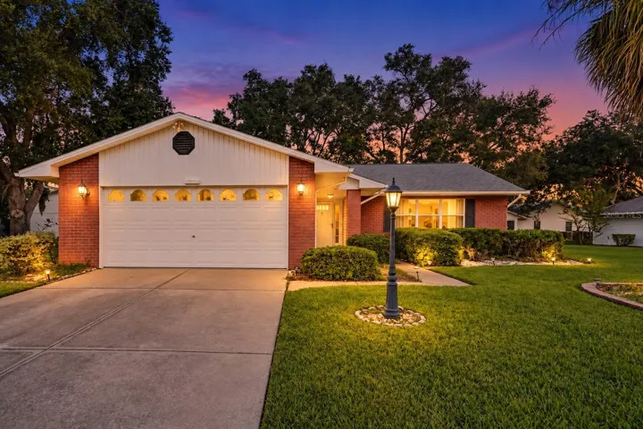 Charming brick home with welcoming front entry, illuminated landscape lighting, and manicured lawn at dusk