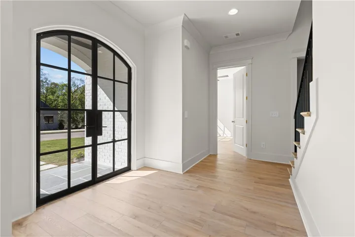 This bright entrance foyer features impressive arched French doors and light hardwood flooring.