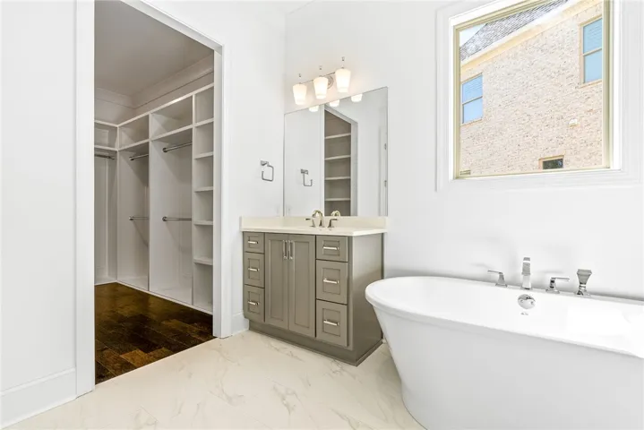 This primary bathroom features a standalone tub, vanity with ample storage, and a well-organized walk-in closet.