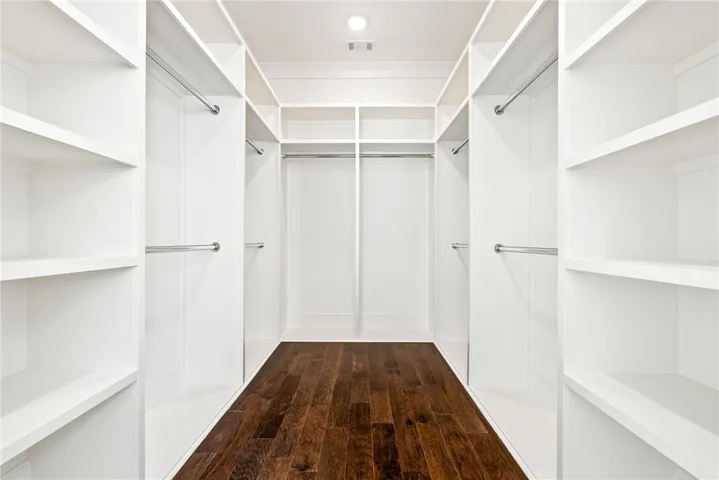 This spacious walk-in closet features ample shelving and dark hardwood flooring.