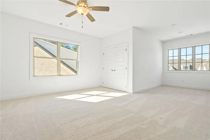 This airy bedroom offers soft carpeting and ample natural light through its generous windows.