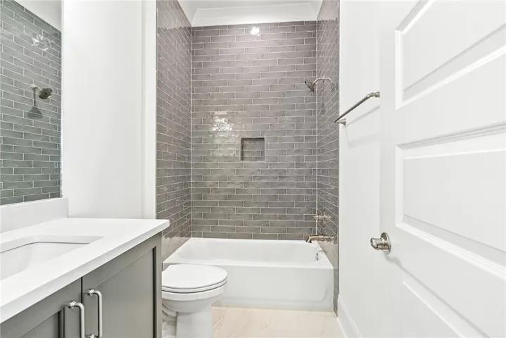 This sleek bathroom features contemporary gray tile work and a pristine white tub, offering a fresh aesthetic.
