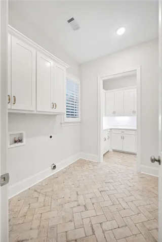 Functional laundry room offers crisp white cabinetry and unique herringbone tile flooring.
