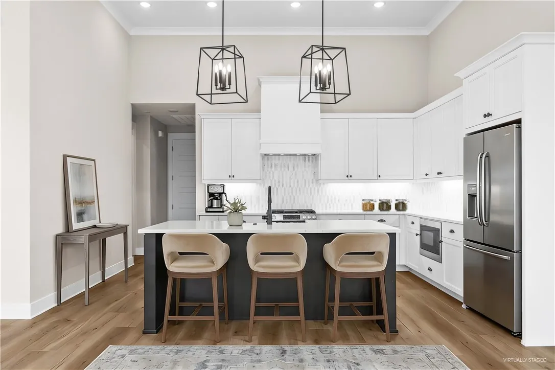 This bright kitchen features high ceilings, an island, and stylish pendant lighting. (virtually staged)