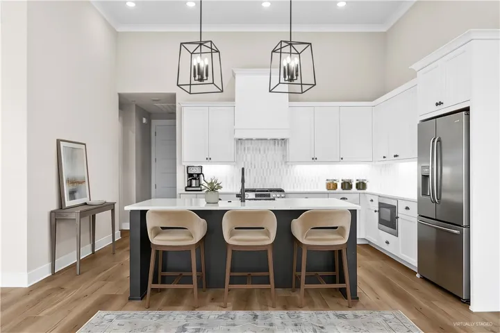 This bright kitchen features high ceilings, an island, and stylish pendant lighting. (virtually staged)