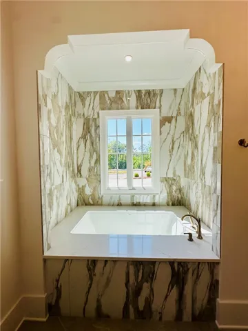 Relax and rejuvenate in this elegant soaking tub, framed by exquisite marble-patterned tile and natural light.