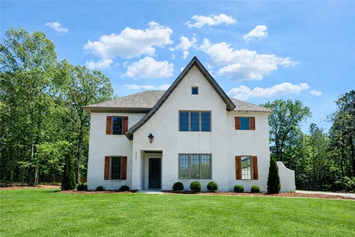 This charming Oxford Cottage features a pristine white brick exterior, set against a vibrant green lawn and mature trees.