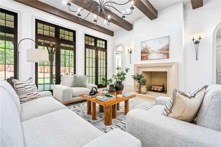 This bright living room features soaring ceilings, a stately fireplace, and expansive glass doors opening to outdoor views.