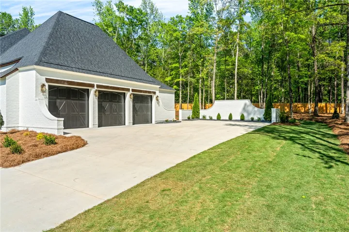 This residence features a multi-car garage with a spacious driveway and lush green surroundings.