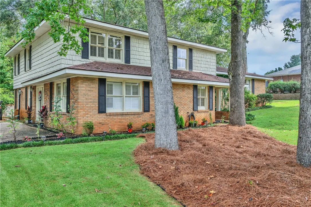 A classic brick and shake-sided home welcomes with lush green lawn and mature trees.