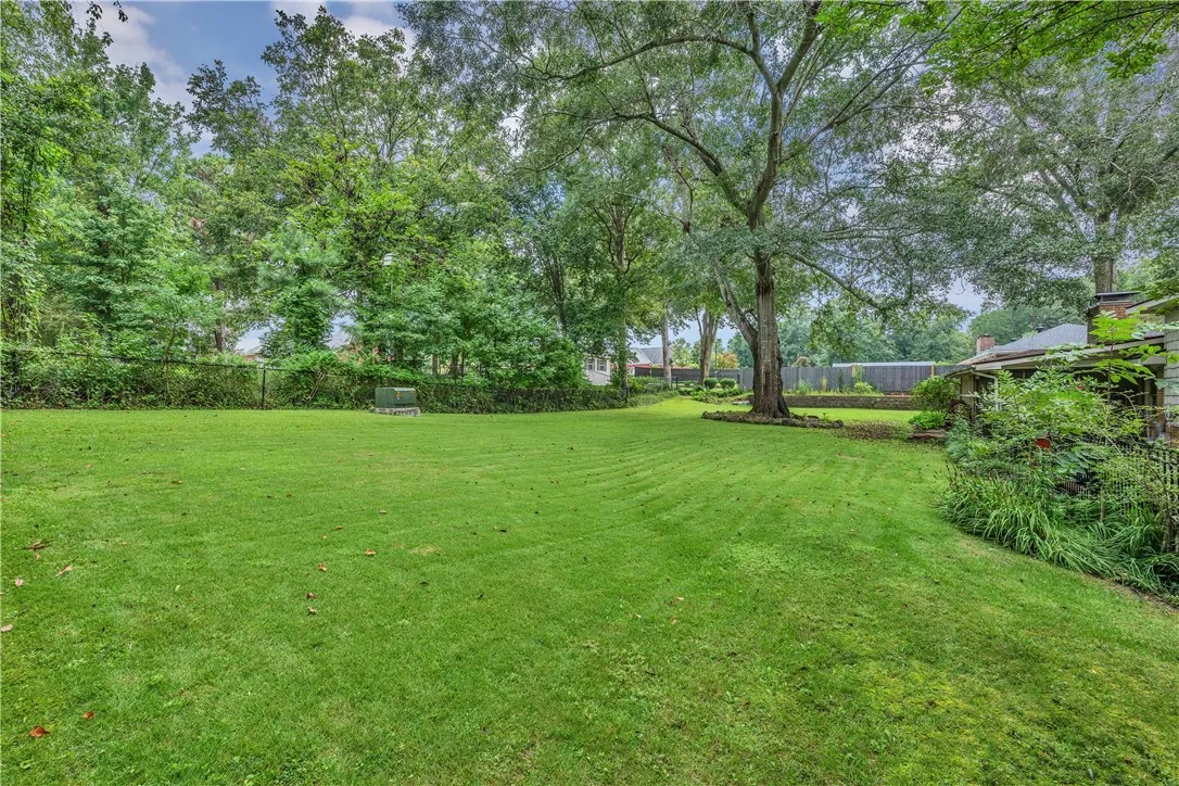 A verdant backyard offers ample space for recreation, bordered by mature trees and a charming brick residence.