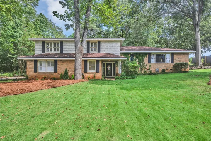 A classic brick and shake siding home framed by mature trees, offering a private yard and inviting entrance.
