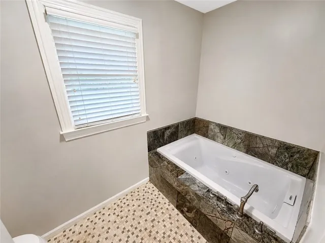 Indulge in a relaxing soak within this jetted tub, encased in elegant stone surround, featuring mosaic tile flooring.