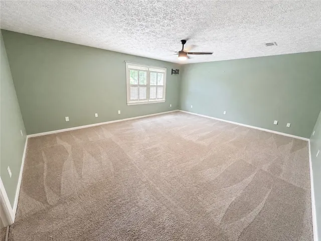 A spacious chamber awaits personalization, complete with soft carpeting and natural illumination from a large window.