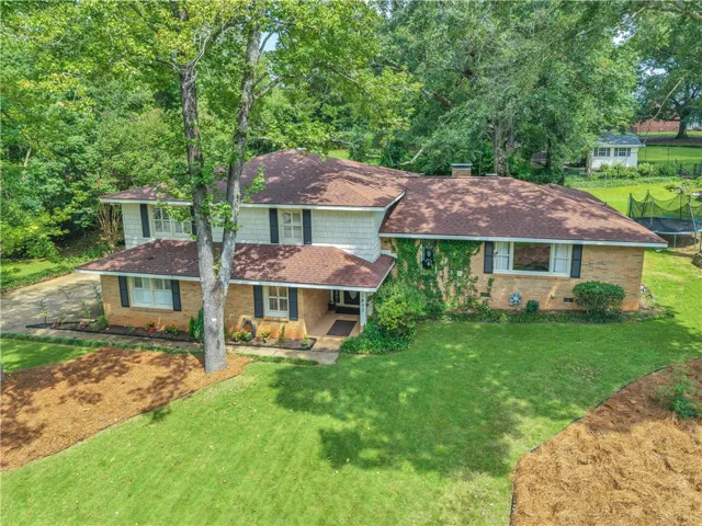 A classic brick and siding residence is nestled amidst mature trees, boasting a well-maintained lawn and welcoming curb appeal.