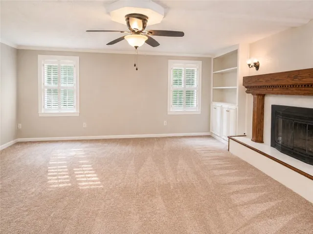A comfortable living space boasts a grand fireplace, built-in shelving, and warm natural light.