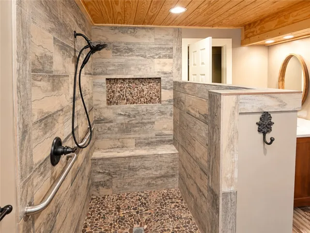 A spacious, naturally illuminated shower features a built-in bench and unique pebble flooring.