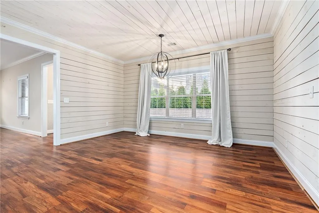 Rich hardwood floors complement the shiplap walls and a striking chandelier illuminates this versatile living space.