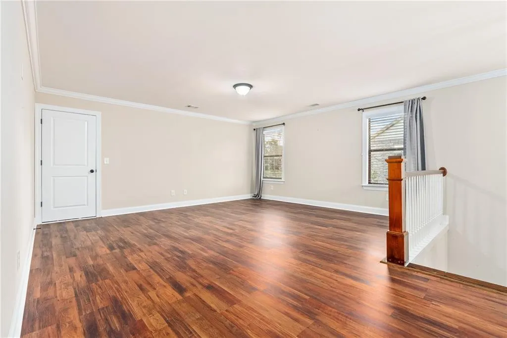 Rich hardwood-style flooring extends across this spacious, naturally illuminated room, perfect for versatile living.