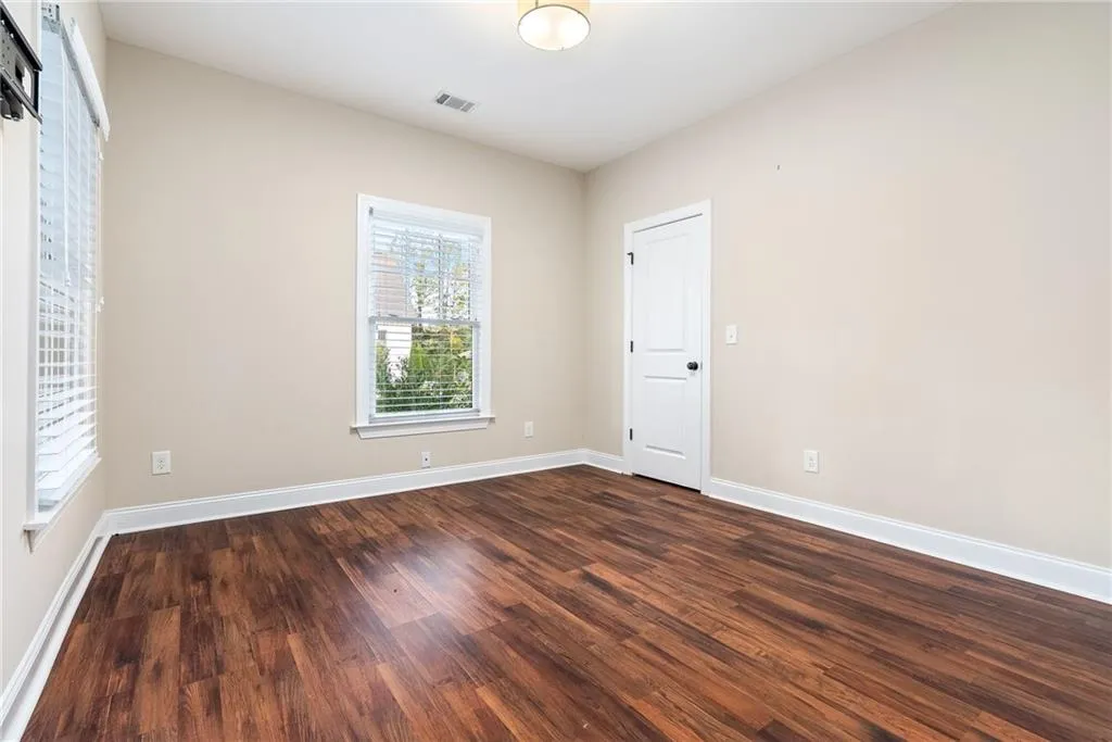 Rich hardwood floors complement the natural illumination from multiple windows in this inviting bedroom.