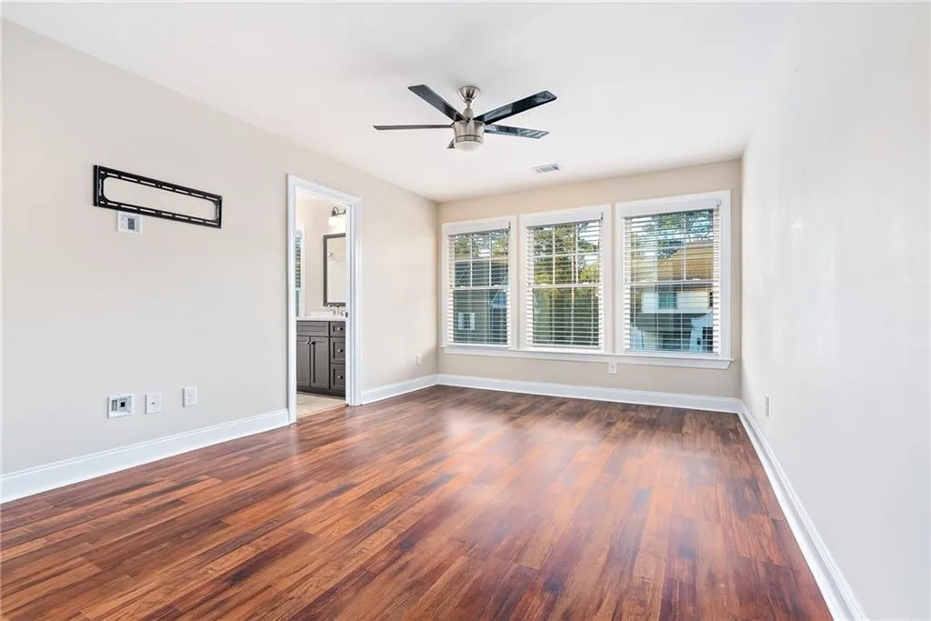 Rich hardwood flooring complements a bedroom with multiple windows and a private bathroom entrance.