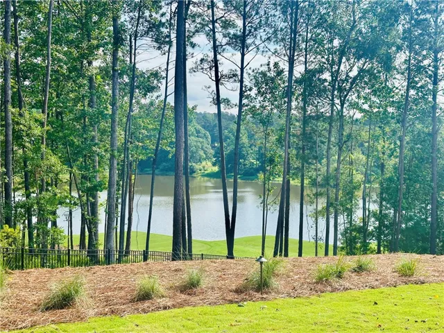 A tranquil lake view unfolds beyond a verdant golf course, framed by towering trees.