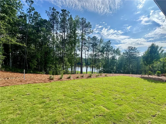 Green lawn slopes towards a serene lake, bordered by a dense forest under a bright sky.