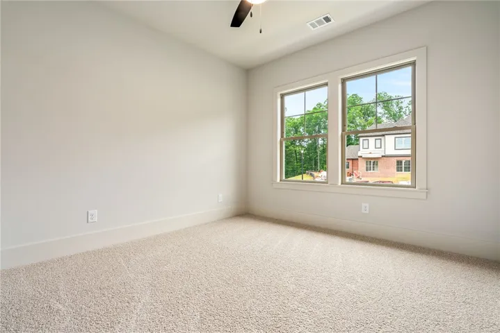 This airy bedroom offers soft carpeting, a ceiling fan, and ample natural light through large windows.
