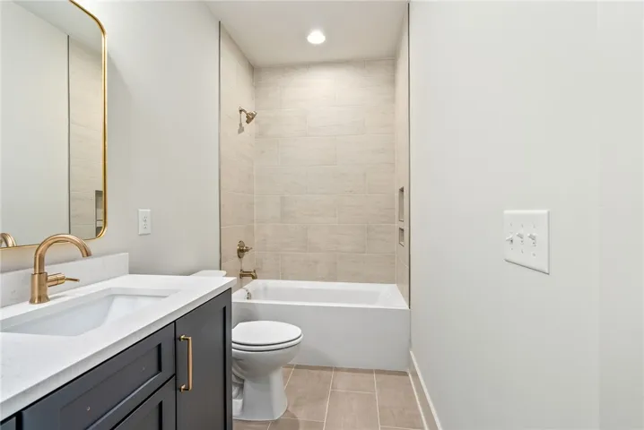 This bathroom features a contemporary vanity with a sleek faucet and a tiled shower-tub combination.