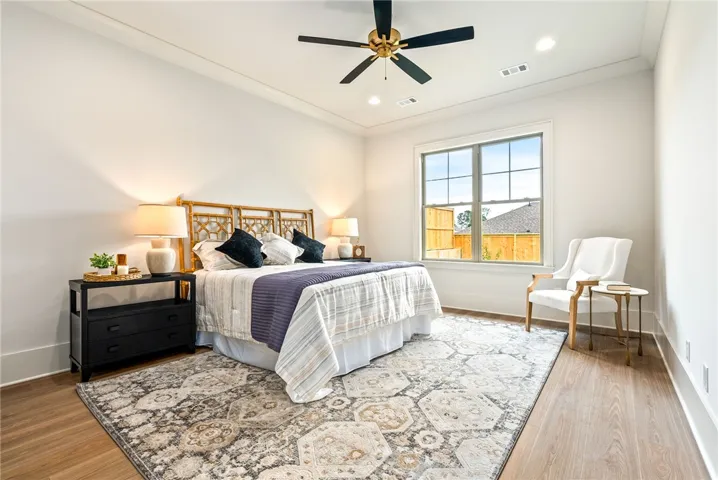This bright bedroom features a ceiling fan, crown molding, and hardwood flooring, offering comfort and style.
