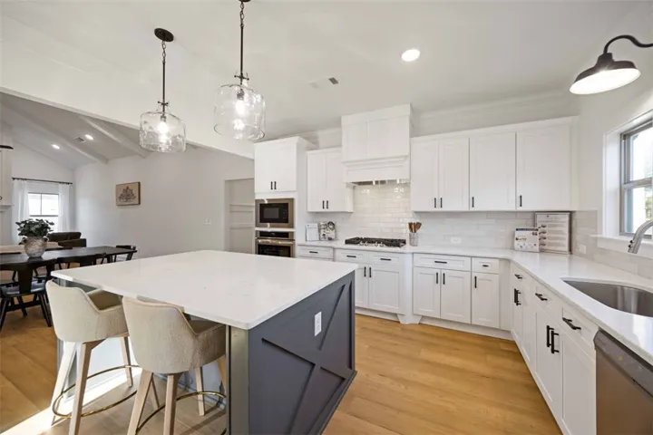 Bright, open kitchen featuring a large quartz island, stainless appliances, and designer glass pendants.