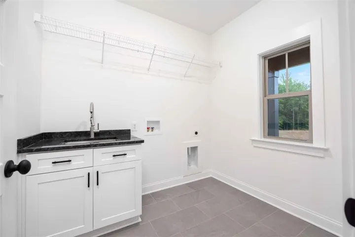 Large laundry room with built-in sink, stone counters, and storage shelving.