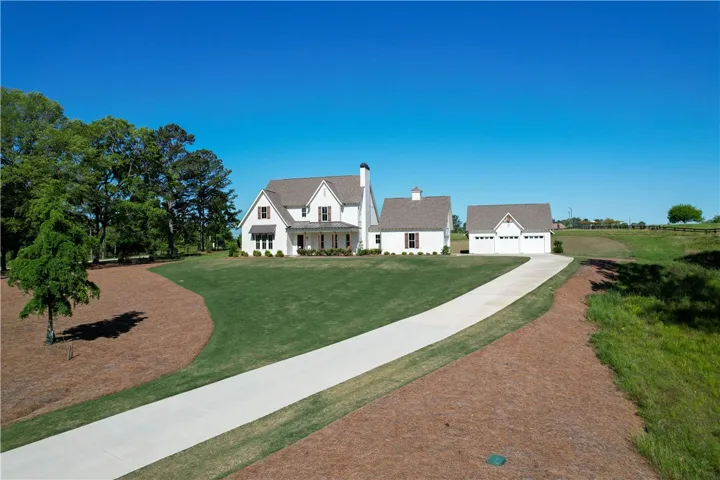 This charming farmhouse-style residence features a generous driveway and expansive green surroundings.