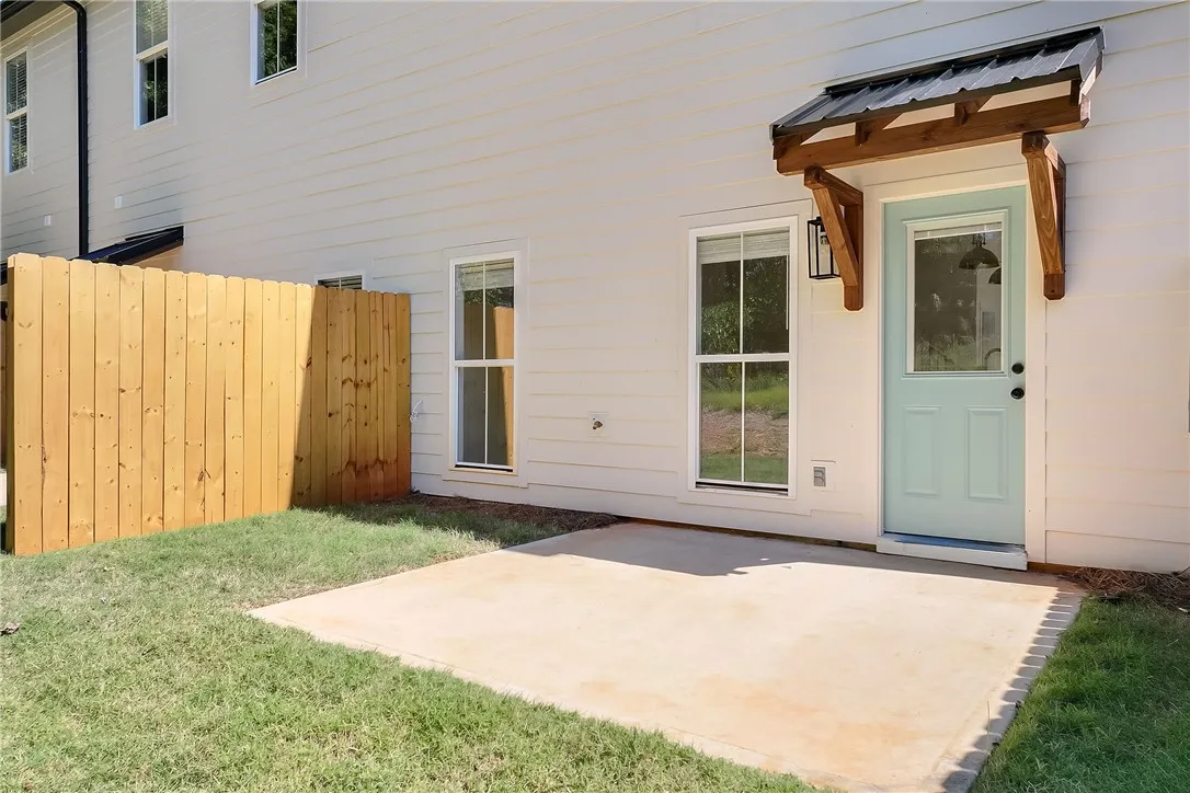 A concrete patio patio sits adjacent to a private grassy yard enclosed by wooden fencing.