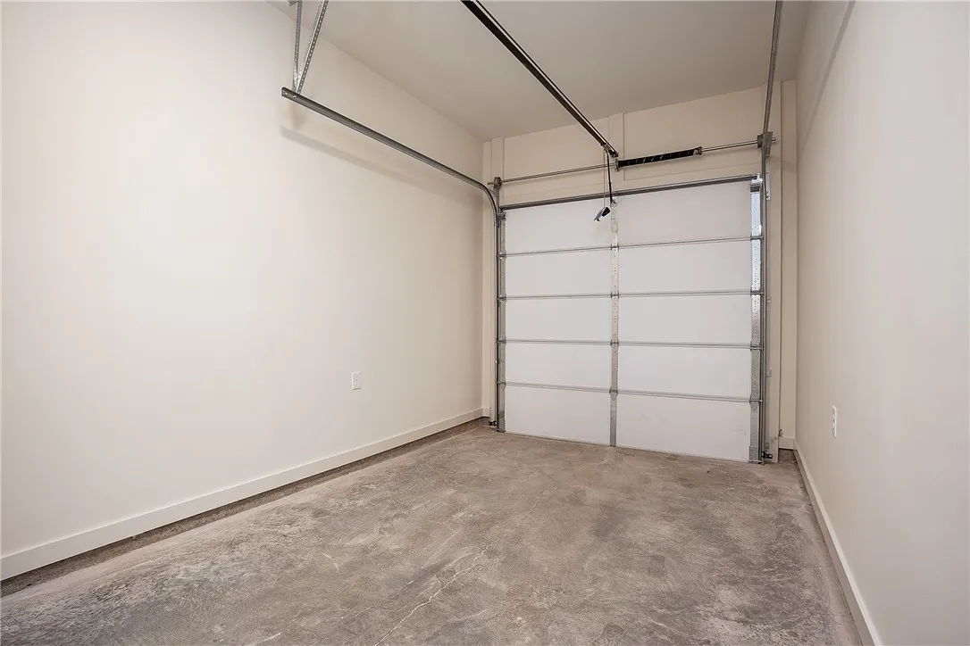 An attached single-car garage features durable concrete flooring and high ceilings.