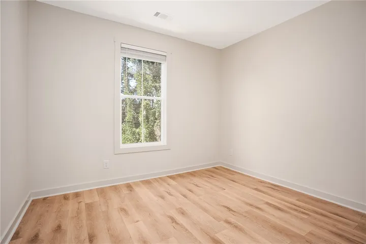A single window overlooks lush trees, illuminating the rich wood-look flooring and clean walls.