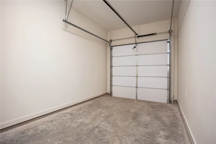 An attached single-car garage features durable concrete flooring and high ceilings.