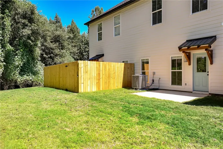 Green lawn spaces border the rear exterior featuring a concrete patio and wooden privacy fencing.
