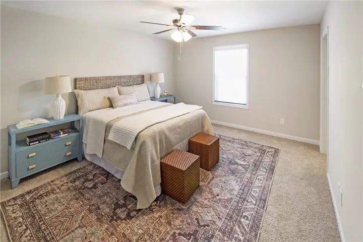 This cozy bedroom features a neutral palette, a large area rug, and a classic ceiling fan for comfort.